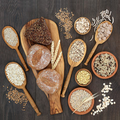 High fibre health food concept with fresh whole grain bread rolls, cereals and grains. Rustic background on oak, top view. 