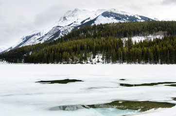 Frozen Mountain Lake with a Snow Capped Mountain in Background on a Cloudy Winter Day. Banff National park, AB, Canada.