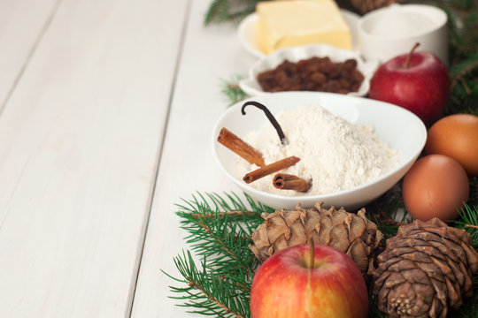Baking ingredients. eggs, butter, spice, apples, raisins, vanilla and cinnamon sticks, white flour and xmas tree on white wooden table background. copy space, new year, xmas, food concept