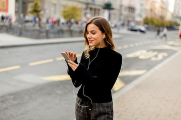 Obraz premium Young brunette woman using mobile while standing on street and waiting for a bus or taxi