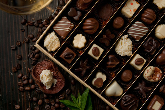 chocolate box of pralines perfect gift for a romantic dinner. Glass of white wine and coffee beans on a wood table and a mint