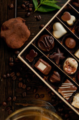 Chocolate box of finest Belgian pralines on a wooden table with a white glass of wine and mnit leaves and coffee beans