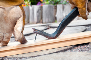 man's hands using a crowbar to remove a nail from a wooden plank