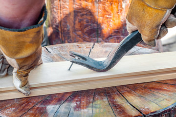 man's hands using a crowbar to remove a nail from a wooden plank