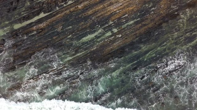 Aerial drone shot of diagonally lined/ shaped rocks with ocean waves rolling over the rocks. Creating a beautiful pattern and texture.