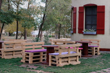 Wooden bench made of pallets for sitting with tables made from coil of electric cable outdoors