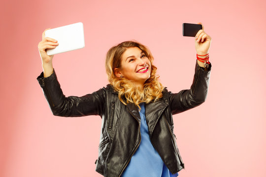 Portrait of a beautiful young woman making selfie both on smart phone and tablet at the same time. Happy young woman photographing herself.