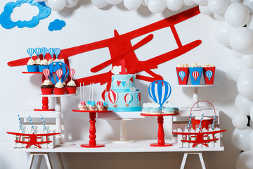 Candy bar on boy's birthday party with a lot of different candies, popcorn, beverages and big cake. Decorated in blue,red and white colors, balloons or aviation theme, indoor