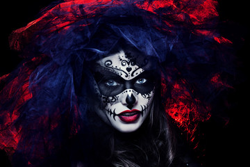 Close up studio portrait of beautiful woman with Halloween sugar skull makeup in red and black colors, wearing bridal veil. Model looking at camera. Dark, dead bride. 
