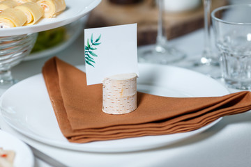Wedding table setting with blank guest card on a dish. Rustic decor in brown tones