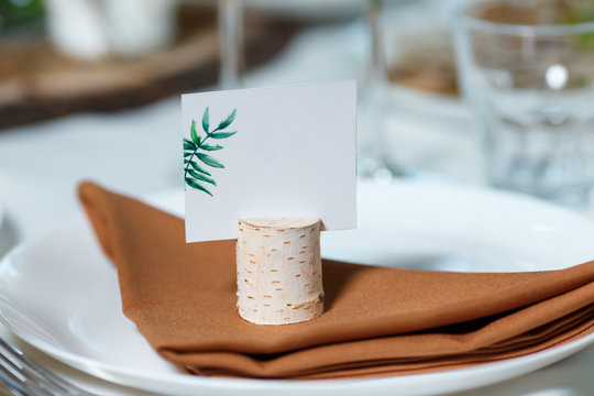 Wedding table setting with blank guest card on a dish. Rustic decor in brown tones