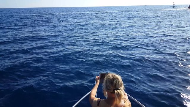 Blond european woman take mobile photos from dolphins in front of boat