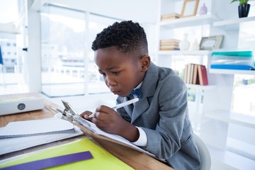 Boy imiting as businessman writing on paper attached to - obrazy, fototapety, plakaty