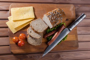 Fried sausages on green salad, bread, cherry tomatoes and cheese on wooden board, top view
