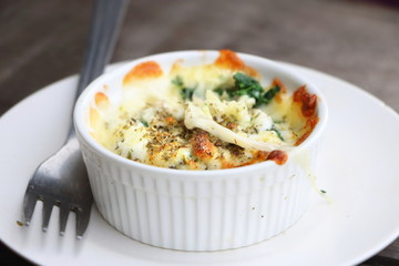 Side view of baked spinach with cheese in white bowl and white plate with fork on wooden table