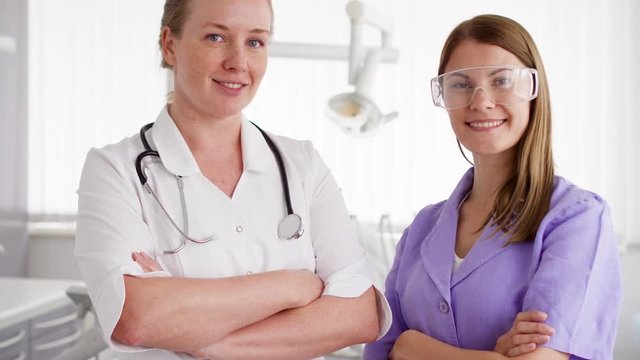 Portrait of two confident professional female doctors standing in hospital room with arms crossed. Women physician with stethoscope and in glasses at work. Health care concept