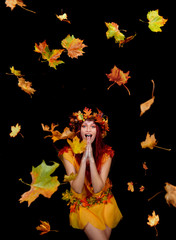 A beautiful young woman dresses up as an Autumn fairy   and wears a wreath on her head made out of Autumn leaves.  She poses for the camera while Autumn leaves fly around her.