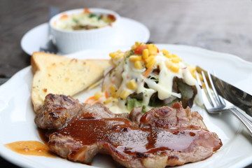 pork steak with sauce and salad vegetables with cream sauce and garlic bread grill in white round plate have fork and knife on wooden table look delicious