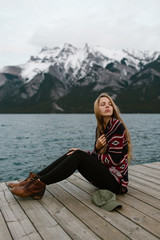Fototapeta na wymiar Sad Young Woman with Long Hair Resting on the Mountain Lake Dock