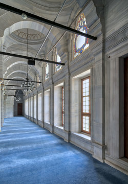 Passage in Nuruosmaniye Mosque, a public Ottoman Baroque style mosque, with columns, arches and floor covered with blue carpet lighted by side windows located in Shemberlitash, Fatih, Istanbul, Turkey