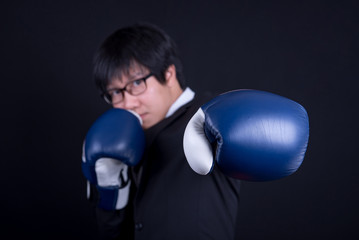 young asian business man wearing suit in boxing punching his left hand pose with black background...