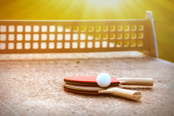 Close up of ping-pong ball with tennis rackets on stone tennis table in sunny lights, Equipment for outdoors table tennis. Outdoor sport concept.healthy lifestyle and objects concept