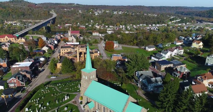 A reverse high angle rising aerial establishing shot of the small town of Brownsville, PA - a Pittsburgh suburb. Bridges over the Monongahela River in the distance.	 	