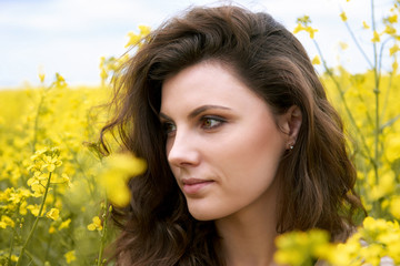 girl face closeup side view, yellow flower on background, spring season, rapeseed field and sky