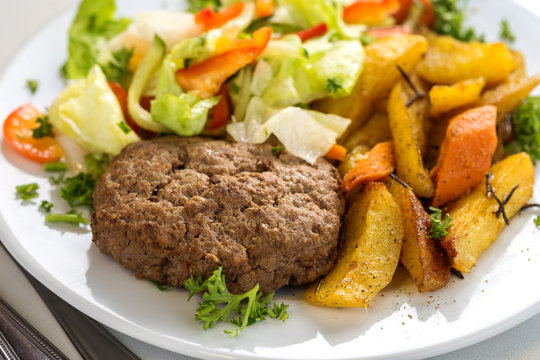 Tasty beef cutlet with salad and potato wedges
