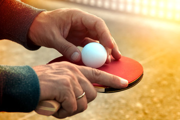 Close up of tennis player hands with tennis racket on nature background in sunny day.Closeup shot of a man serving in table tennis. Outdoor tennis table play