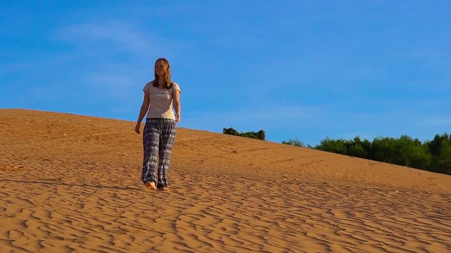 Slowmotion shot of a young girl in asian pants walks along the sand of the red desert