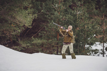 Female hunter in camouflage clothes ready to hunt, holding gun and walking in forest.