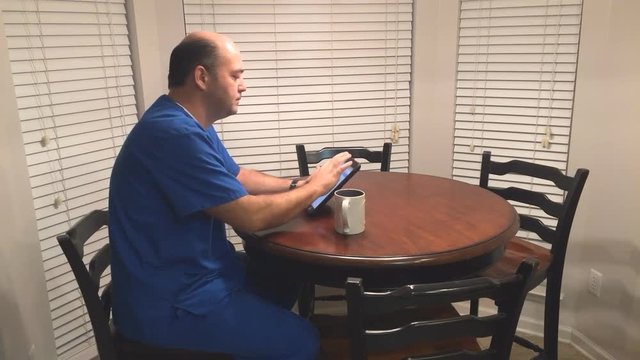 Busy male nurse using tablet computer at breakfast table before heading off to work.