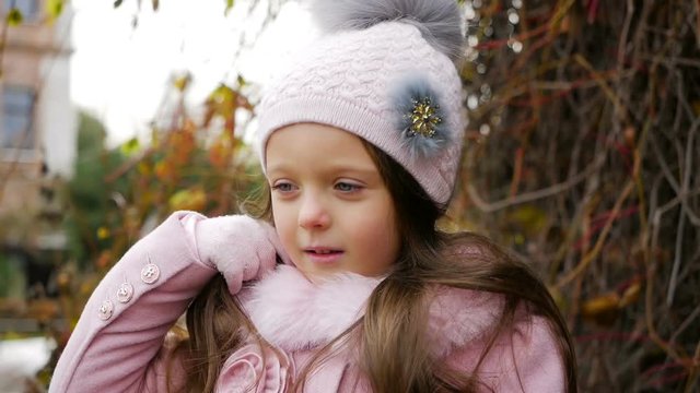 baby girl lying on autumn leaves in pink coat and hat