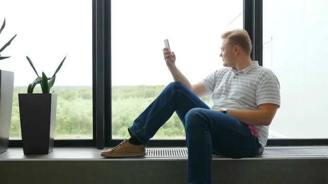 Man writes an SMS and looks out the airport window. The guy is talking in messengers. A young man in a smartphone plays games. A guy writes a text message to a girl and dreams. scrolling pictures phon