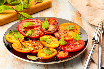 Black plate of salad with sliced tomatoes served on wooden table