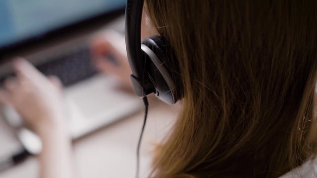 Crop woman working as office assistant using laptop and headphones