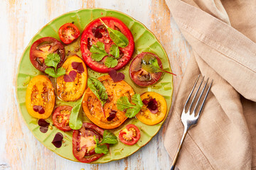 Green plate of salad with sliced tomatoes served on wooden table