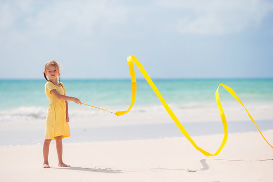 Adorable little girl dancing with yellow gymnastic ribbon on the beach