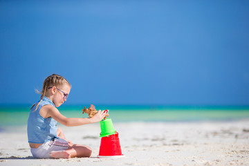 Little girl at tropical white beach making sand castle