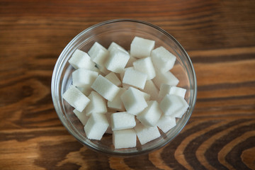 White sugar cubes in glass on wooden background 