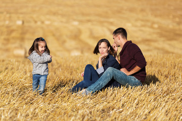 Naklejka na ściany i meble Happy young family with 2 year old girl in a harvested field