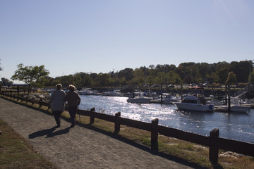 two people walking on a path with boats in the background