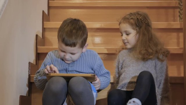 Little children plays on tablet sitting on staircase