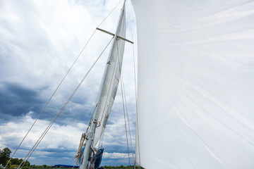 Fototapeta premium yacht mast with a white sail, the yacht moves with a sail, white sail against a background of cloudy sky