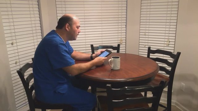 Busy male nurse drinking coffee and looking at tablet computer before heading off to work.