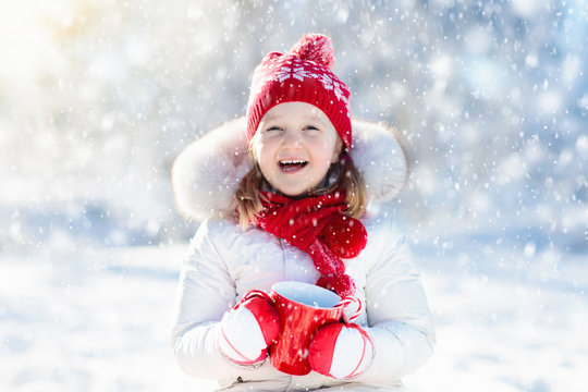 Child Drinking Hot Chocolate In Winter Park. Kids In Snow On Christmas.