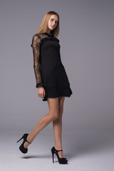 Naklejka premium Full length portrait of a serious trendy woman in black dress standing isolated on a gray background