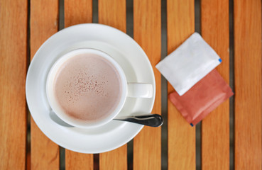 Cup of hot Chocolate with sugar envelopes on the wood table. Top view.
