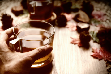 Female hands holding cup of tea from rose hip tea and bouquet of rose hips and chestnuts, autumn leaves on the wooden background.Seasonal, vitamin drink.Autumn background.